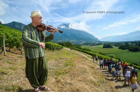 photographe tourisme sur une balade gourmande : un musicien violoniste accueille les promeneurs lors de la balade gourmande en Combe de Savoie, avec en arrière-plan la dent d'Arclusaz