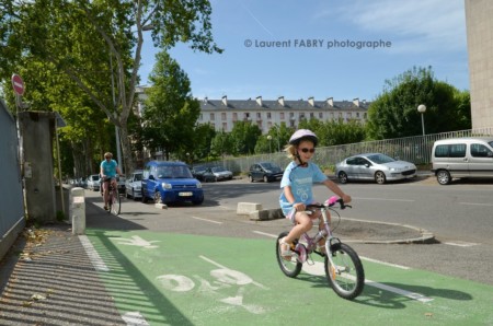 Photographe urbanisme à Chambéry : une petite fille portant le casque et les lunettes de soleil roule sur une piste cyclable près de la gare de Chambéry