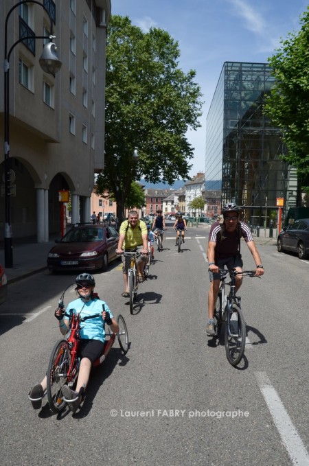 Photographe urbanisme à Chambéry : des cyclistes dont l'un d'entre eux sur un vélo couché, circulent dans la rue devant le Manège