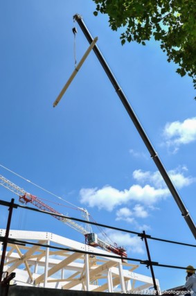 photographe de chantier à Aix-les-bains : vue verticale d'une poutrelle en bois suspendue au bout de la grue