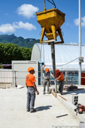 photographe de chantier à Aix-les-bains : des ouvriers remplissent des coffrages de béton depuis un godet apporté par la grue