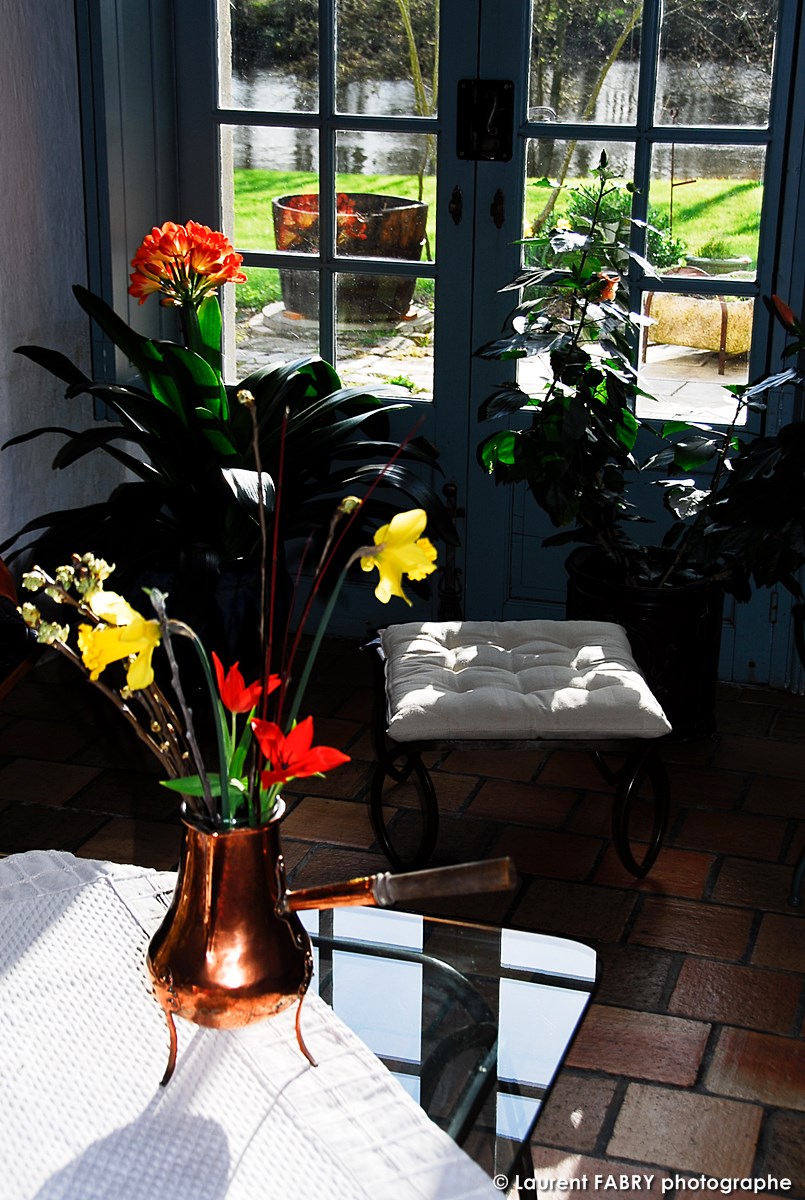 vue directe sur le jardin de la maison d'hôtes et la rivière depuis le salon et son mobilier en fer forgé (chocolatière, tabouret et table basse)