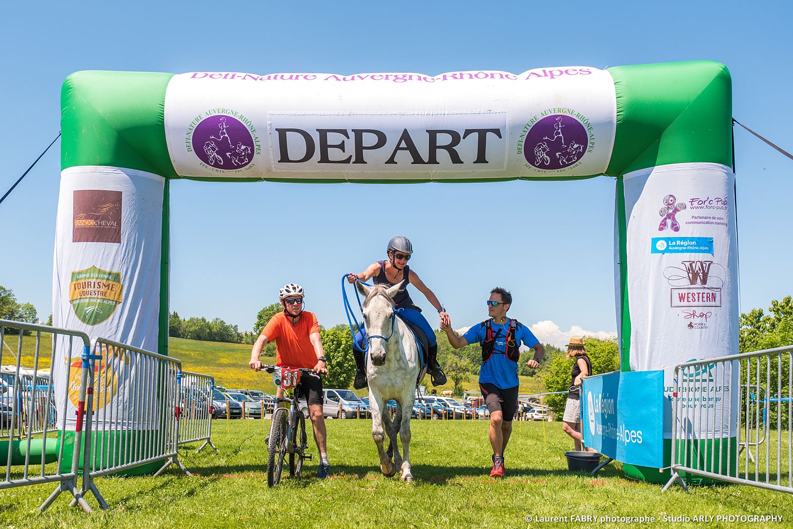 Cycliste, coureur à pieds et cavalier sous l'arche de départ du raid multi-sport en Haute Savoie