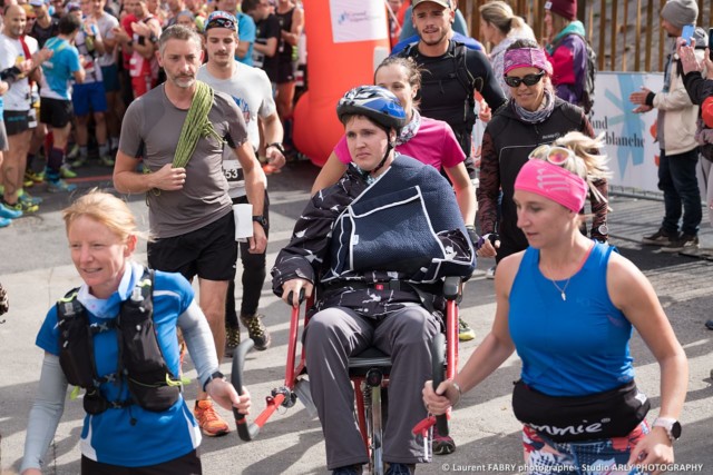 Départ d'une personne à mobilité réduite (PMR) dans un fauteuil porté par des coureurs